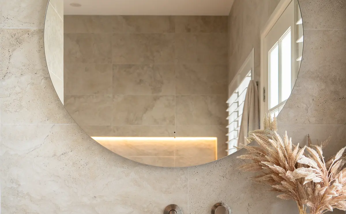 A calm bathroom in large stone-look tile with a round mirror and a lit niche