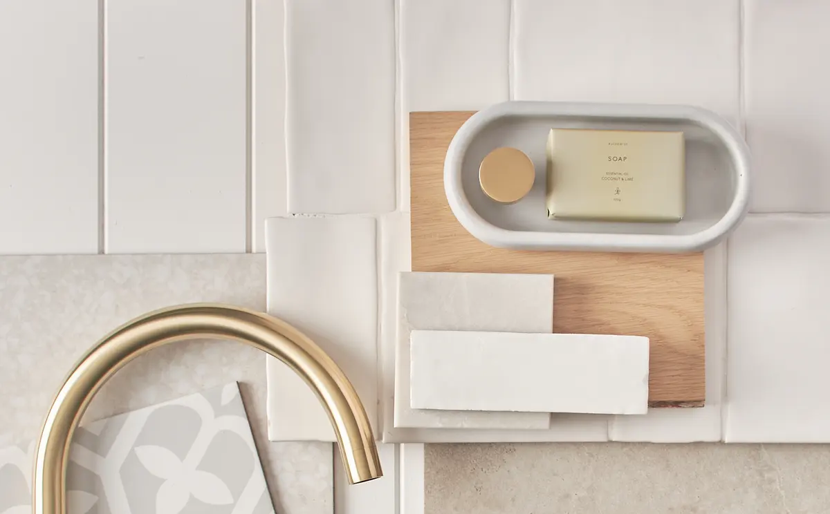 A brushed-brass faucet laid over tile, wood and stone samples