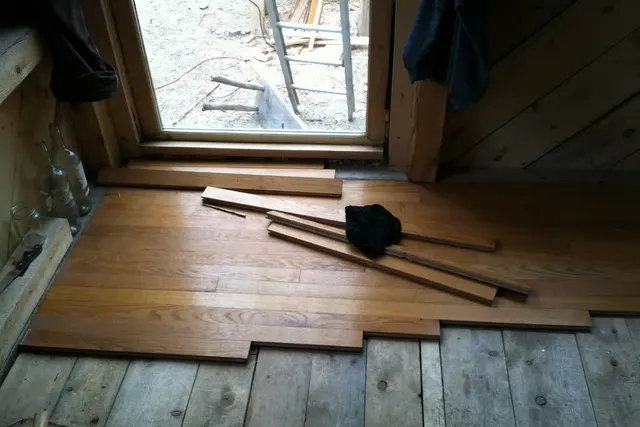 New hardwood boards being laid across an old pine floor