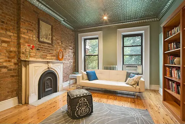 A brownstone parlor with exposed brick, a marble mantel and a tin ceiling